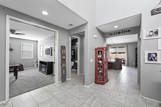 corridor featuring light carpet, baseboards, visible vents, and light tile patterned flooring