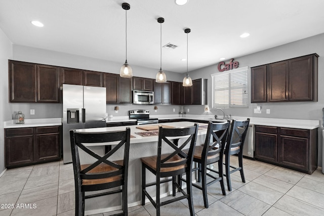 kitchen featuring a kitchen island, decorative light fixtures, stainless steel appliances, dark brown cabinets, and light countertops