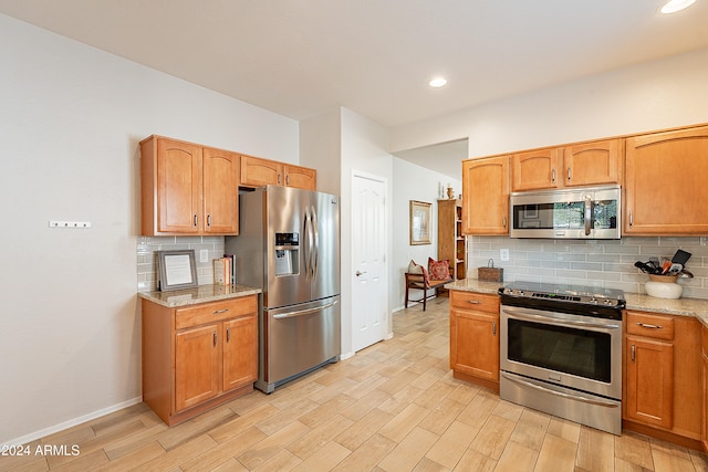 kitchen featuring backsplash, light wood-type flooring, light stone countertops, and stainless steel appliances