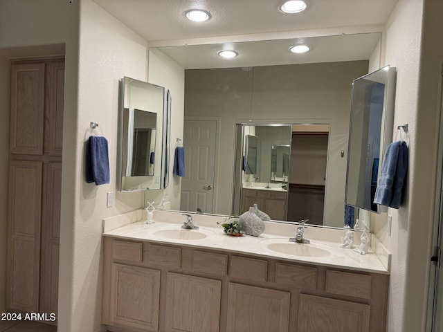 full bathroom featuring double vanity, a textured wall, and a sink