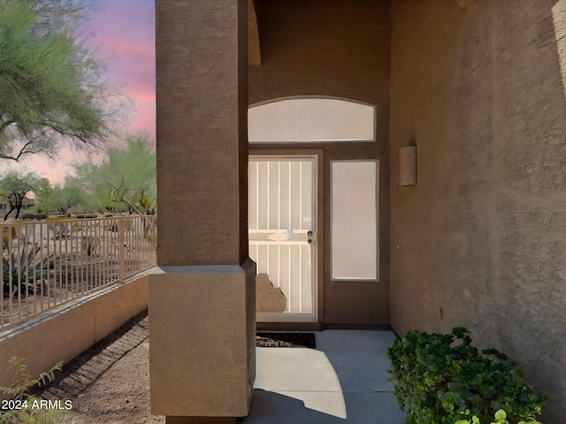 exterior entry at dusk featuring a balcony and stucco siding