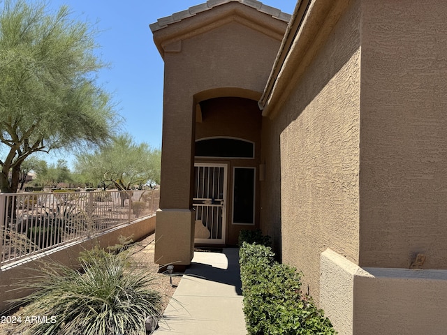 view of exterior entry with fence and stucco siding