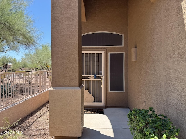 view of exterior entry featuring fence and stucco siding