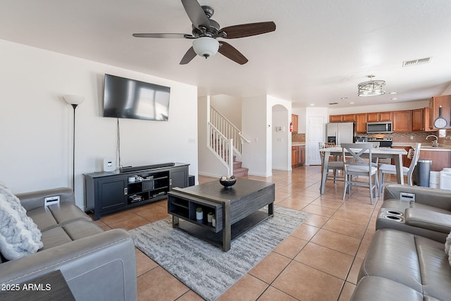living room with light tile patterned floors, visible vents, stairway, arched walkways, and ceiling fan