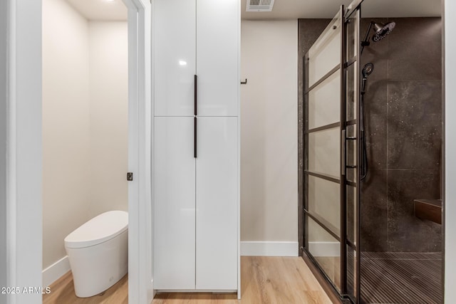 bathroom with wood-type flooring, a tile shower, and toilet