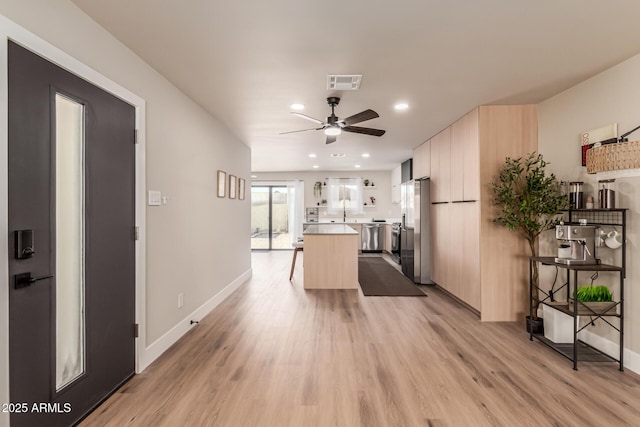 kitchen featuring ceiling fan, appliances with stainless steel finishes, a kitchen island, light brown cabinetry, and light wood-type flooring