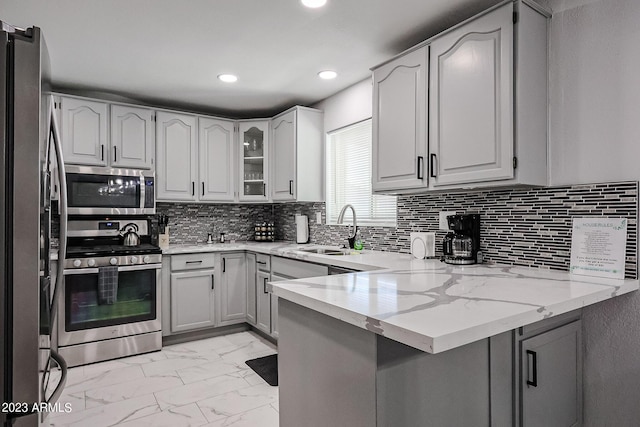 kitchen featuring light stone countertops, a peninsula, a sink, appliances with stainless steel finishes, and marble finish floor