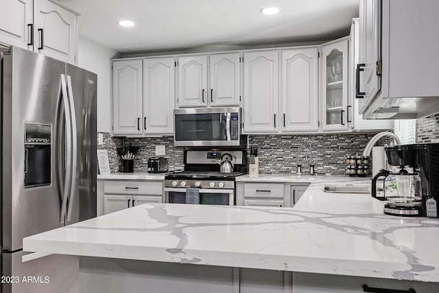 kitchen with light stone countertops, a sink, glass insert cabinets, appliances with stainless steel finishes, and backsplash