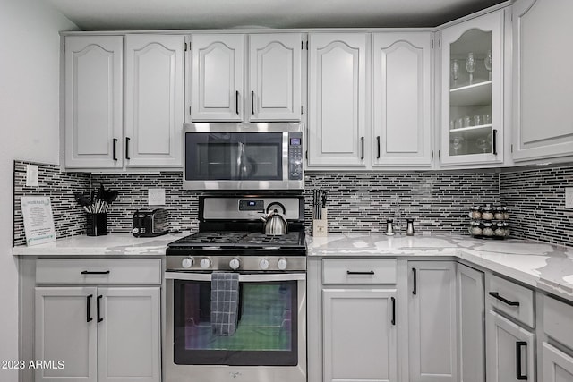 kitchen with glass insert cabinets, backsplash, appliances with stainless steel finishes, and white cabinetry