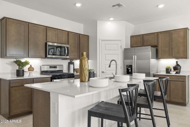 kitchen with appliances with stainless steel finishes, a breakfast bar area, a center island with sink, and dark brown cabinets