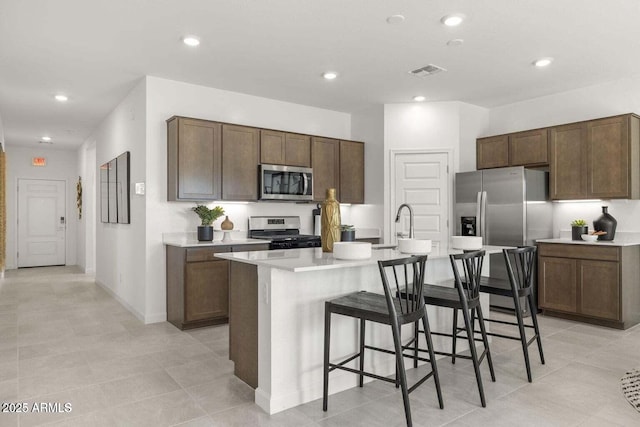 kitchen with appliances with stainless steel finishes, a kitchen bar, an island with sink, and dark brown cabinets