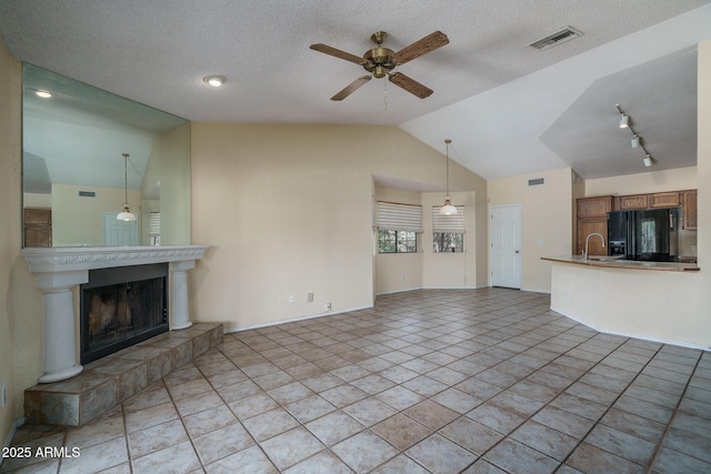 6101 E Beck Ln, Scottsdale, AZ 85254 - unfurnished living room featuring vaulted ceiling, ceiling fan, a tiled fireplace, a textured ceiling, and rail lighting