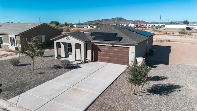 ranch-style house featuring central air condition unit, a mountain view, a garage, and solar panels