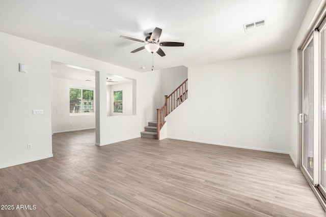unfurnished living room with a ceiling fan, visible vents, baseboards, light wood-style floors, and stairs