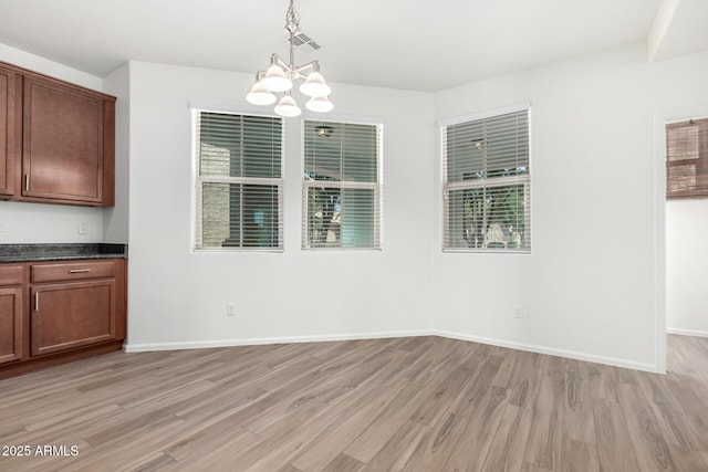 unfurnished dining area with an inviting chandelier, baseboards, light wood finished floors, and visible vents