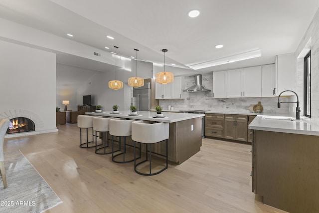 kitchen featuring wall chimney exhaust hood, sink, white cabinetry, a center island, and pendant lighting