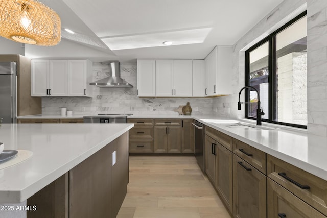 kitchen featuring wall chimney exhaust hood, decorative light fixtures, appliances with stainless steel finishes, decorative backsplash, and white cabinets