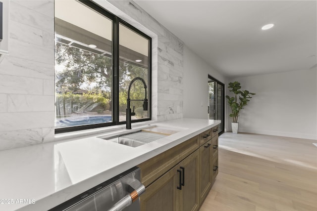 bar featuring tasteful backsplash, sink, stainless steel dishwasher, plenty of natural light, and light wood-type flooring