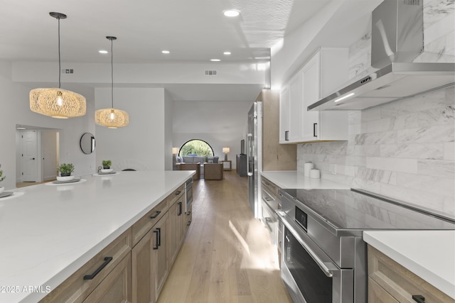 kitchen featuring stainless steel electric range oven, pendant lighting, white cabinets, wall chimney range hood, and light wood-type flooring