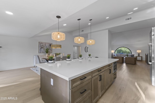 kitchen with a spacious island, lofted ceiling, decorative light fixtures, light hardwood / wood-style flooring, and stainless steel microwave