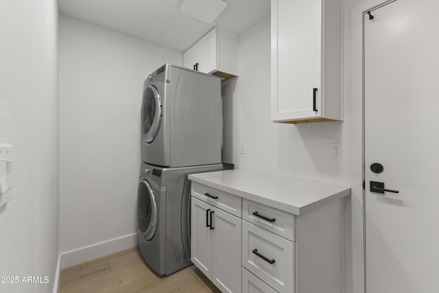 clothes washing area with cabinets, stacked washing maching and dryer, and light hardwood / wood-style flooring