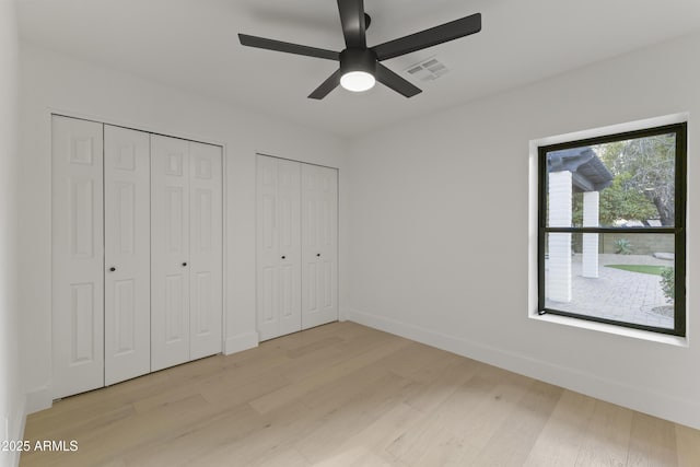 unfurnished bedroom featuring ceiling fan, light hardwood / wood-style flooring, and multiple closets