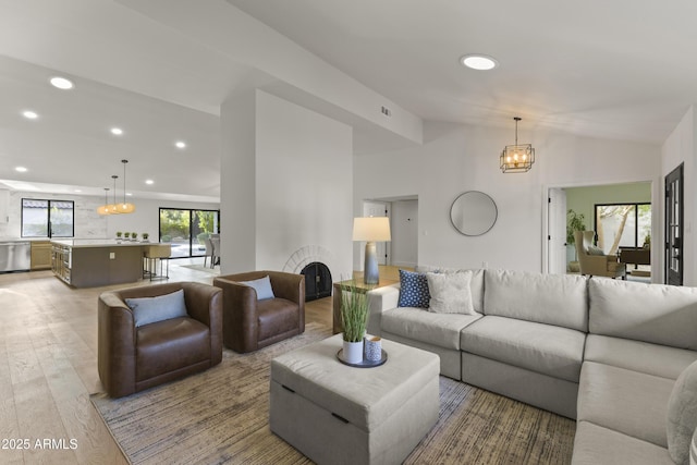 living room featuring a notable chandelier, vaulted ceiling, and light hardwood / wood-style floors