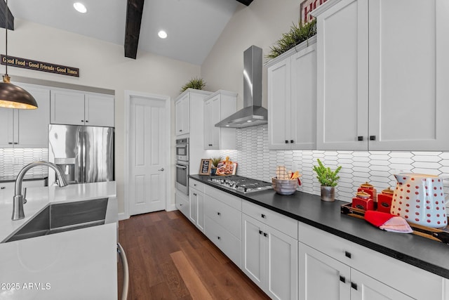 kitchen featuring a sink, dark countertops, appliances with stainless steel finishes, and wall chimney range hood