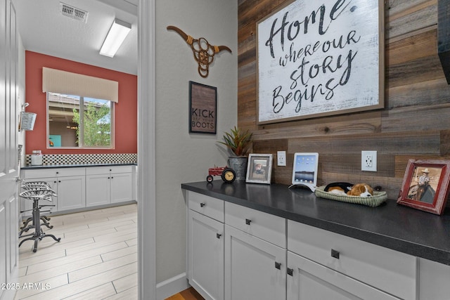 interior space with visible vents, backsplash, dark countertops, white cabinets, and light wood finished floors