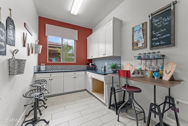 kitchen featuring decorative backsplash, dark countertops, and white cabinetry