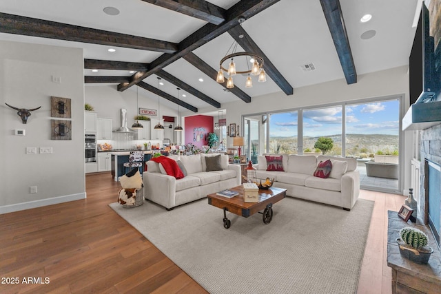 living area featuring visible vents, a chandelier, lofted ceiling with beams, a fireplace, and wood finished floors