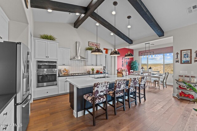 kitchen with visible vents, dark wood-style floors, stainless steel appliances, wall chimney exhaust hood, and a sink