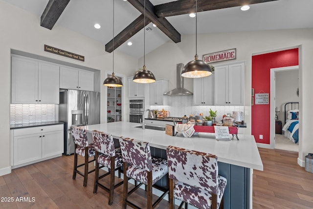 kitchen featuring a breakfast bar, lofted ceiling with beams, dark wood-style flooring, stainless steel appliances, and wall chimney range hood