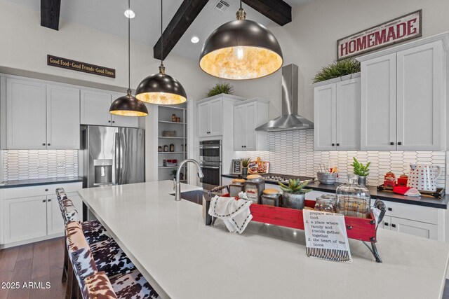 kitchen featuring visible vents, an island with sink, appliances with stainless steel finishes, beamed ceiling, and wall chimney exhaust hood