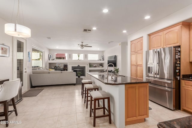 kitchen with a kitchen bar, light brown cabinetry, a ceiling fan, a sink, and stainless steel fridge