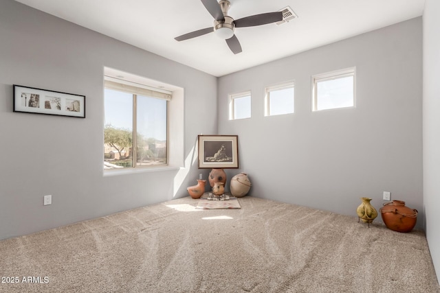 carpeted empty room featuring visible vents, a healthy amount of sunlight, and a ceiling fan