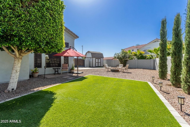 view of yard featuring a fenced backyard, an outdoor fire pit, a storage shed, an outdoor structure, and a patio area