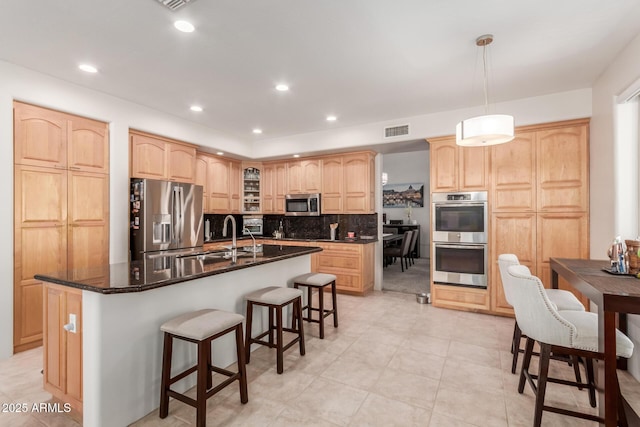 kitchen with visible vents, light brown cabinetry, a breakfast bar area, stainless steel appliances, and a sink