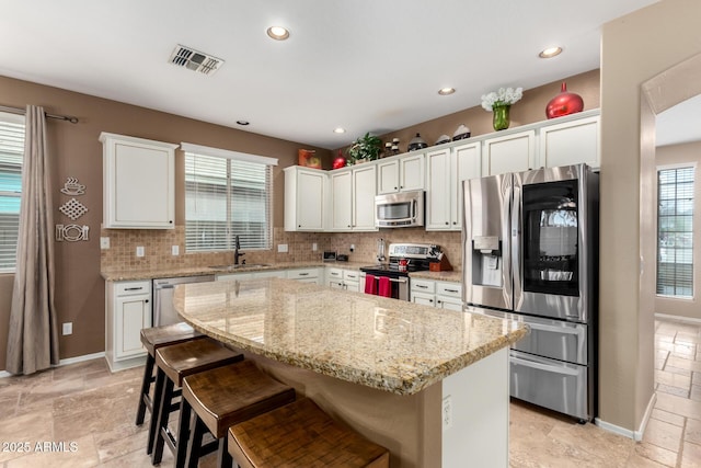 kitchen with light stone countertops, white cabinets, appliances with stainless steel finishes, a kitchen island, and a breakfast bar area