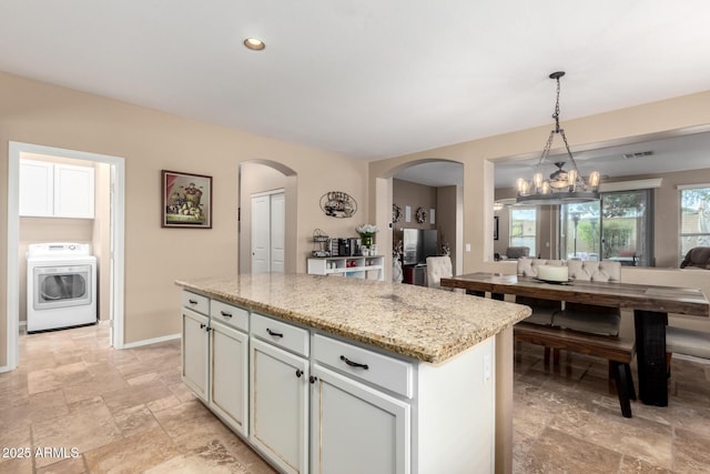 kitchen with light stone countertops, washer / dryer, a kitchen island, hanging light fixtures, and a notable chandelier