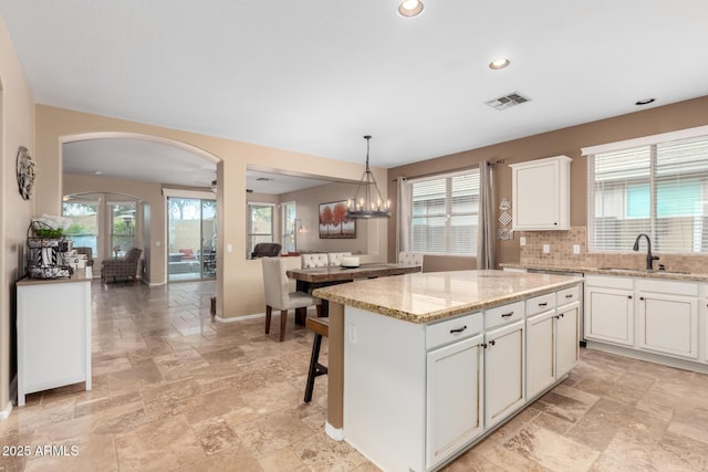 kitchen featuring white cabinetry, sink, light stone countertops, pendant lighting, and a center island