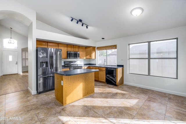 kitchen with brown cabinets, dark countertops, a kitchen island, appliances with stainless steel finishes, and lofted ceiling