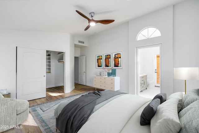 bedroom with visible vents, a ceiling fan, ensuite bathroom, wood finished floors, and vaulted ceiling