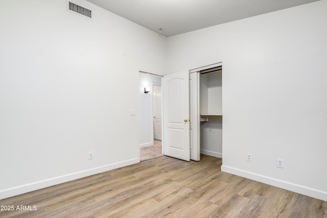 unfurnished bedroom with wood finished floors, visible vents, a closet, and baseboards