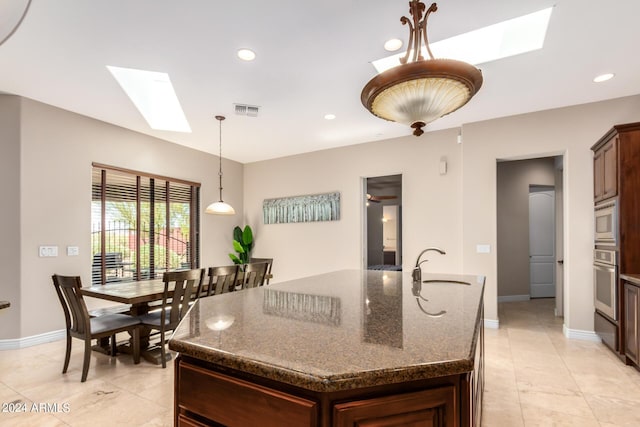 kitchen with sink, a kitchen island with sink, a skylight, stainless steel appliances, and dark stone counters