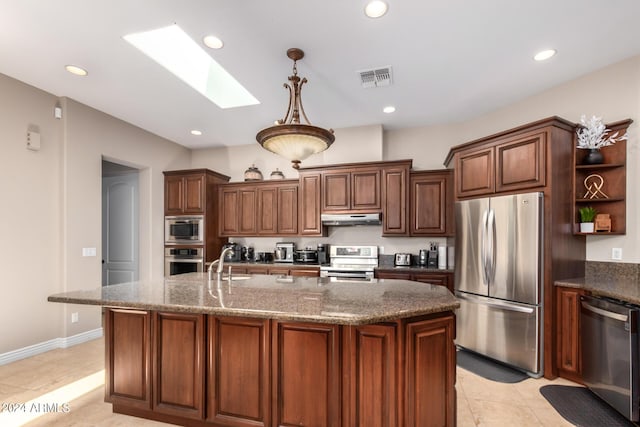 kitchen featuring sink, a skylight, dark stone countertops, appliances with stainless steel finishes, and an island with sink