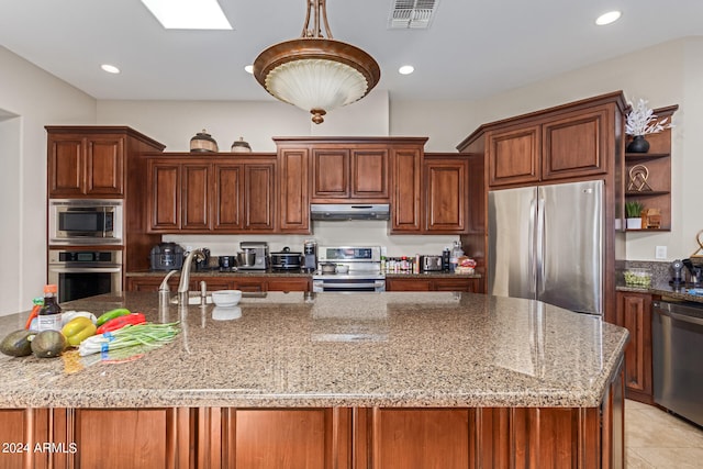 kitchen featuring sink, appliances with stainless steel finishes, a skylight, light stone counters, and decorative light fixtures