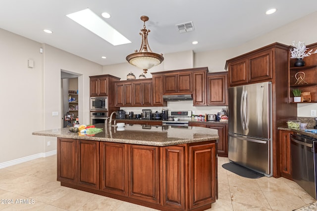 kitchen with decorative light fixtures, a skylight, dark stone countertops, stainless steel appliances, and a center island with sink