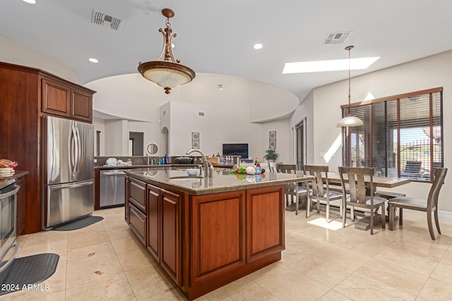 kitchen featuring appliances with stainless steel finishes, decorative light fixtures, an island with sink, sink, and dark stone counters