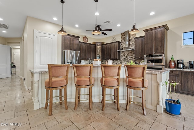 kitchen featuring wall chimney exhaust hood, stainless steel appliances, light stone counters, and a kitchen island